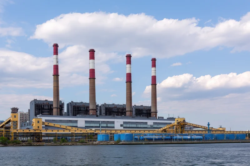 Large urban power plant with red-and-white smokestacks viewed from across the water