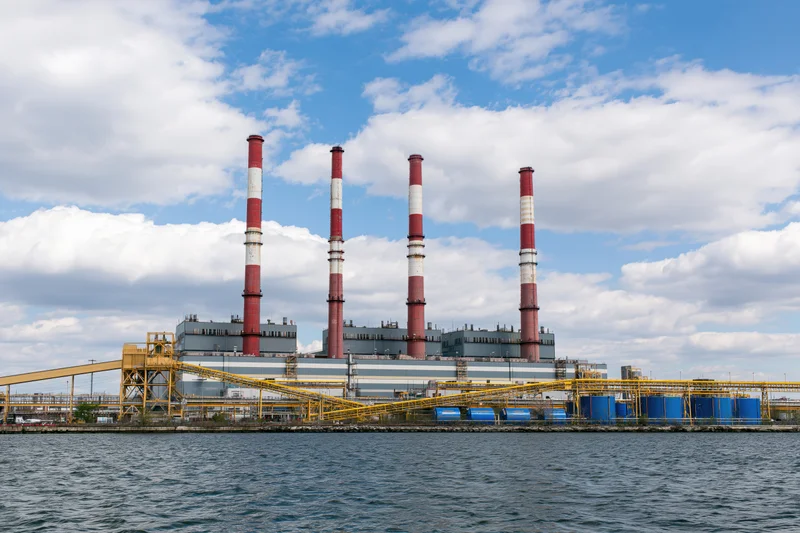 Large power plant with red and white smokestacks viewed from across the water