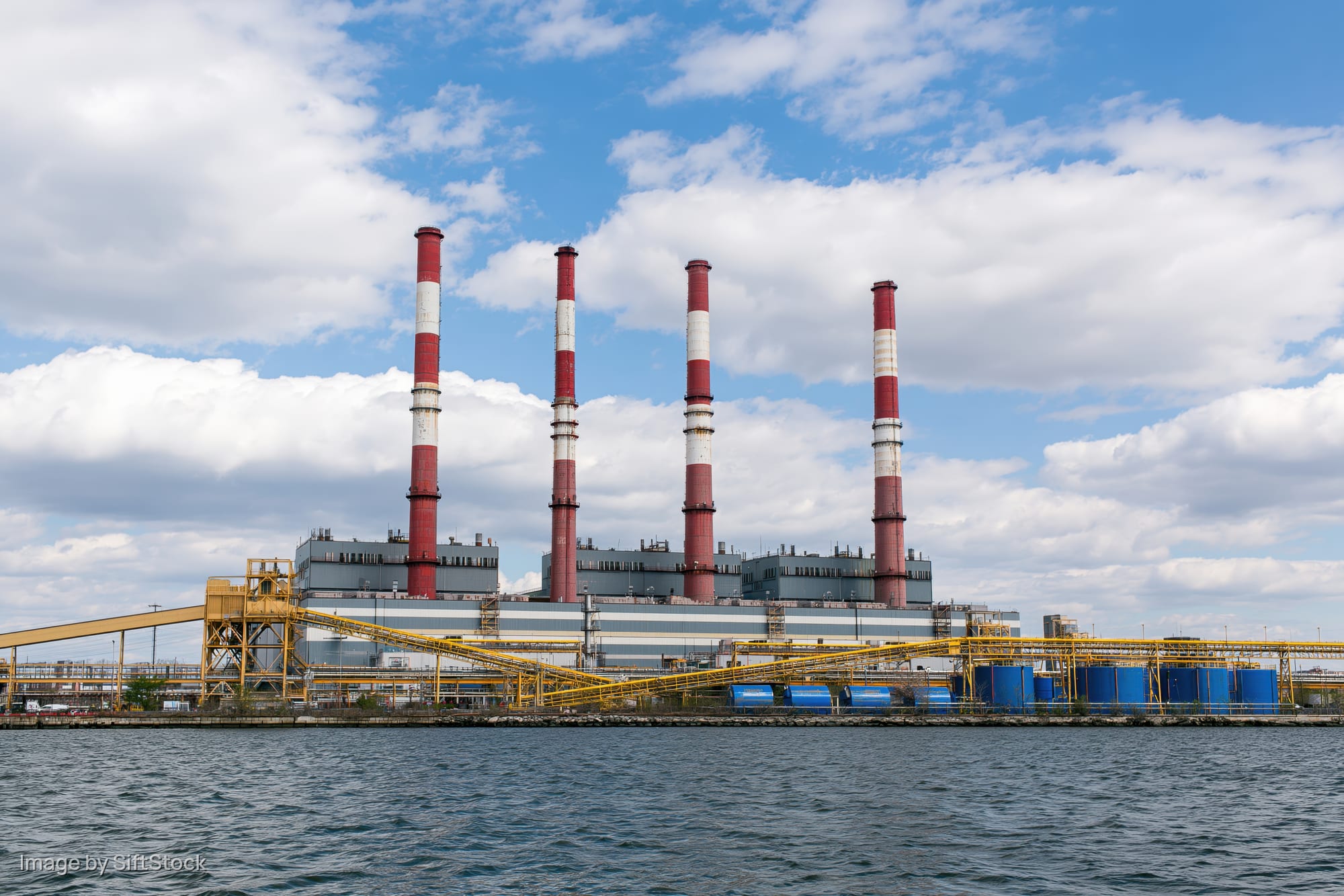 Large power plant with red and white smokestacks viewed from across the water