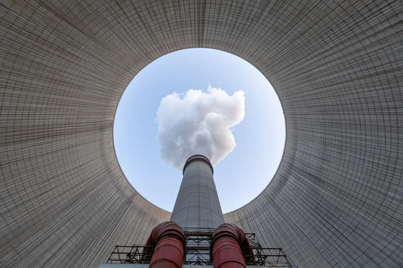 View from inside a cooling tower looking up at a smoke-emitting chimney against the sky