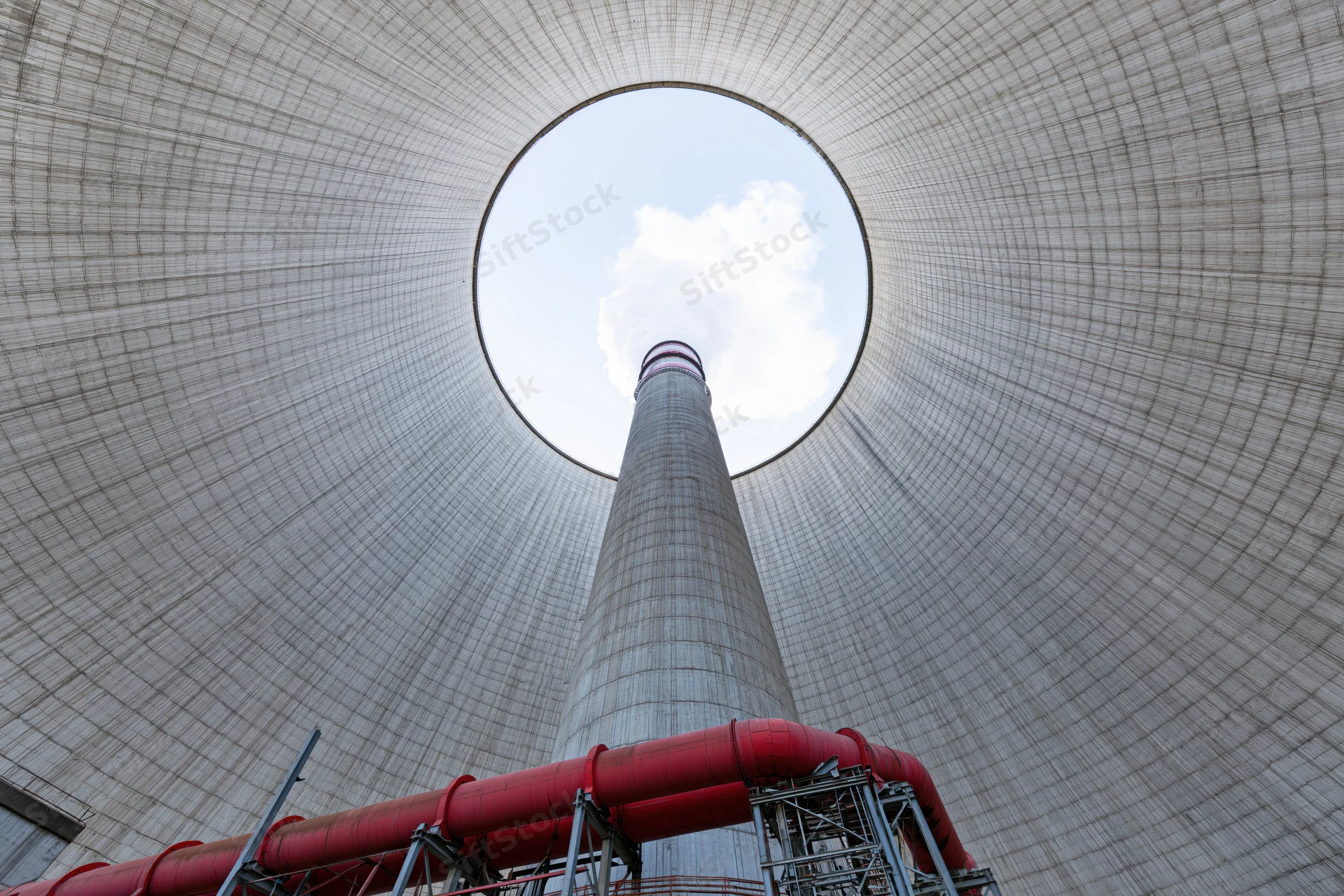 View from inside a massive concrete cooling tower looking up at the smokestack and sky