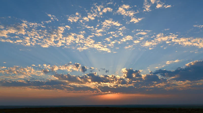 Sunset sky with scattered clouds and sun rays above low horizon