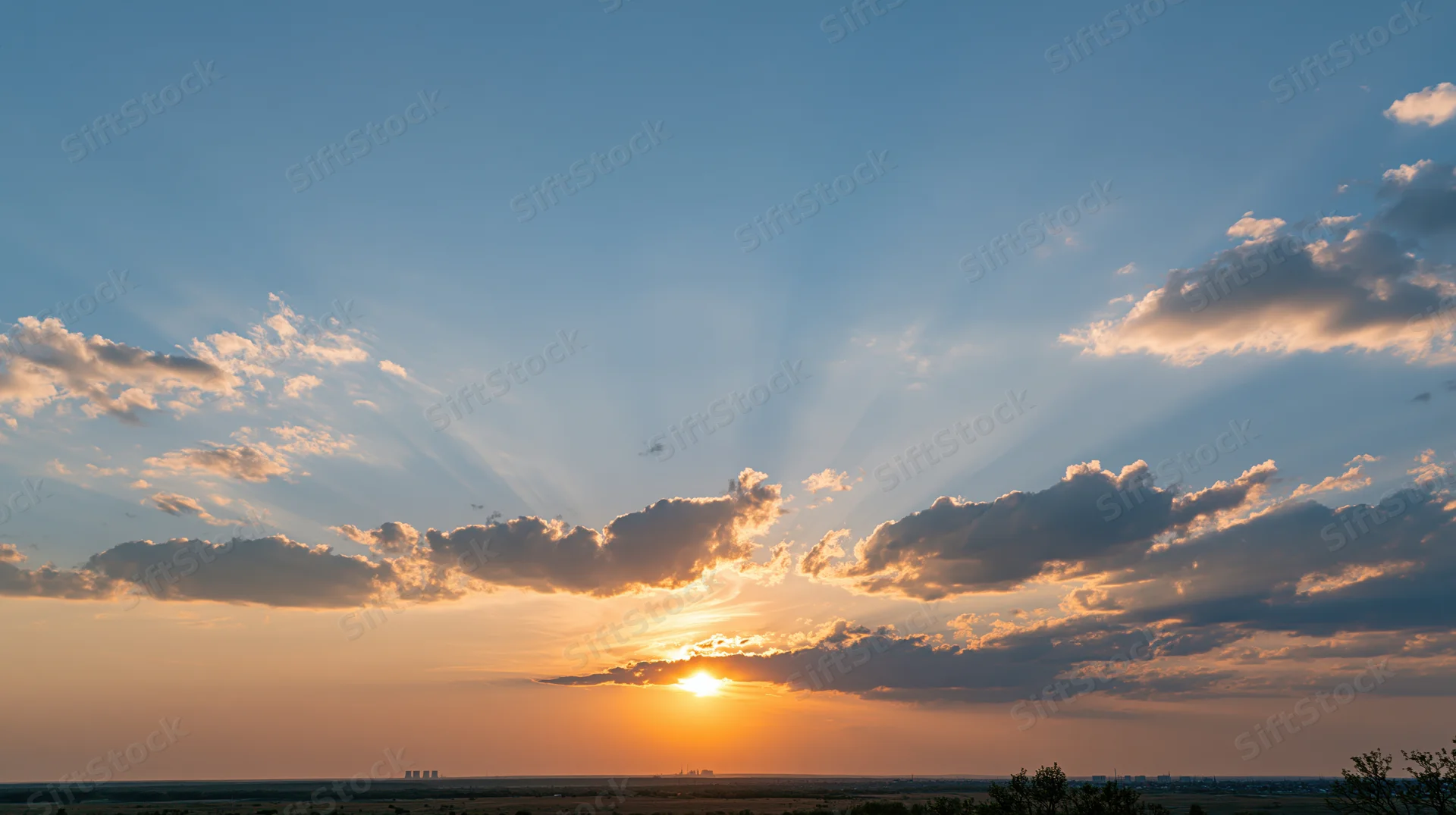 Sunset over a low horizon with scattered clouds and sunbeams in the sky