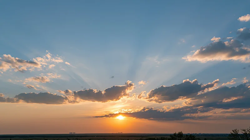 Sunset over a low horizon with scattered clouds and sunbeams in the sky