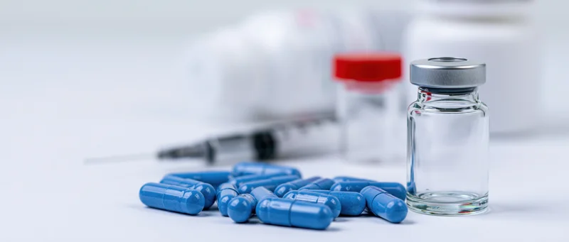 Blue capsules and glass vial with syringe on white surface