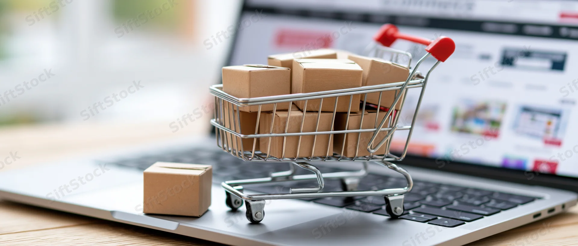 Miniature shopping cart filled with cardboard boxes on laptop keyboard with online store in background