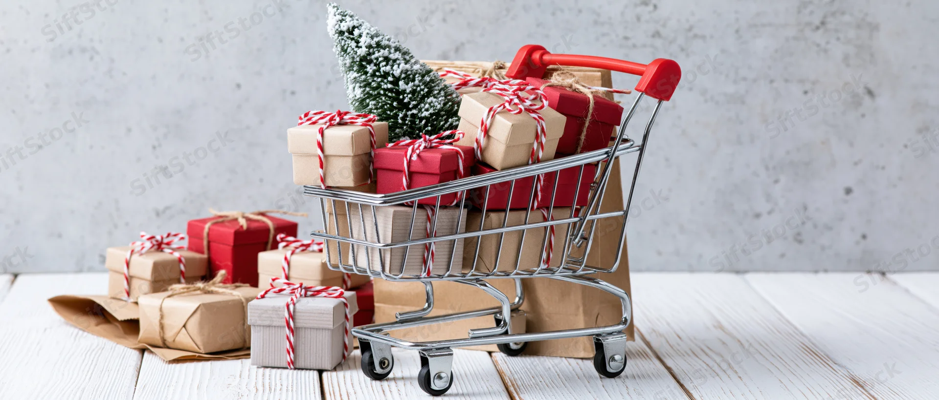 Miniature shopping cart filled with wrapped gifts and a small christmas tree on a wooden surface