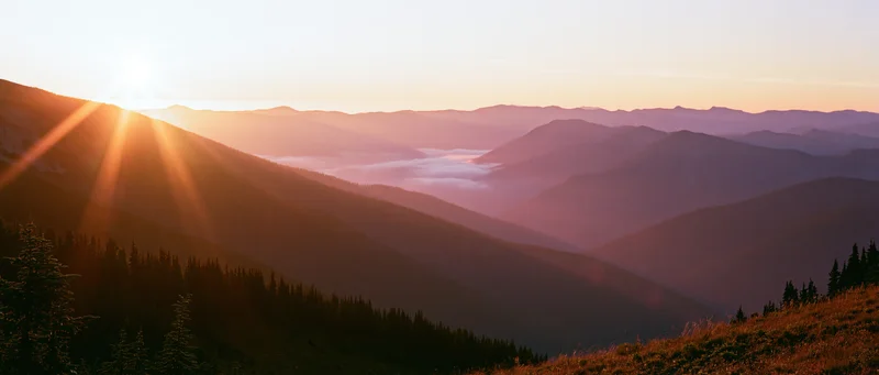 Mountain ridgelines receding into the distance at sunset with forested slopes and misty valleys below