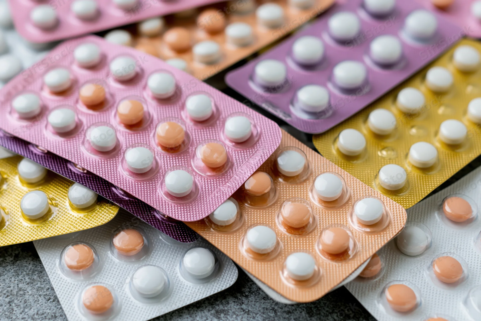 Multiple blister packs of oral contraceptive pills layered on a textured surface