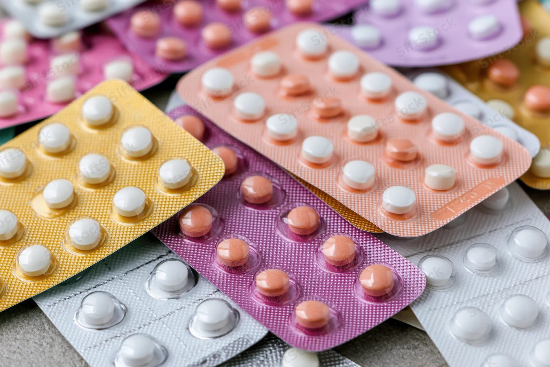 Multiple blister packs of oral contraceptive pills layered on a textured surface