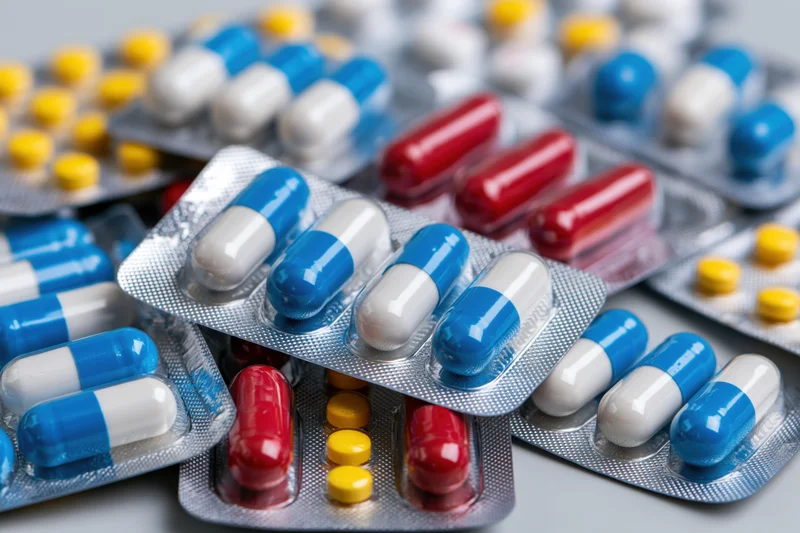 Multiple blister packs of pharmaceutical capsules and tablets arranged in close-up view on a neutral surface