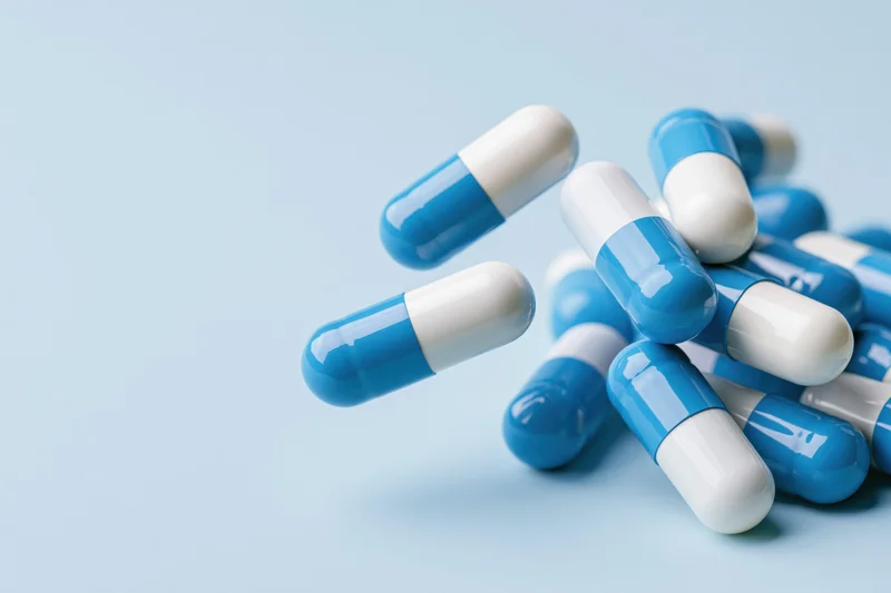Blue and white pharmaceutical capsules scattered on a light blue surface with copyspace