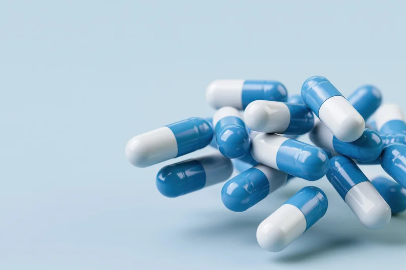 Blue and white pharmaceutical capsules scattered on a light blue surface with copyspace
