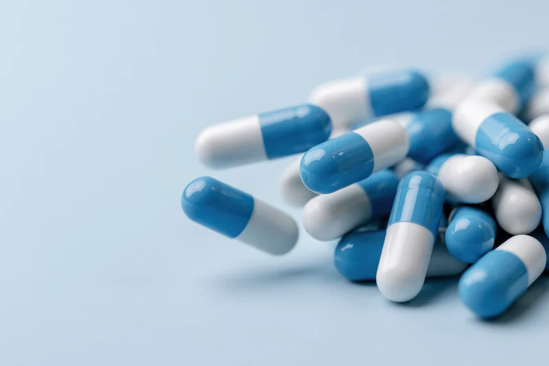 Blue and white pharmaceutical capsules scattered on a light blue surface with copyspace