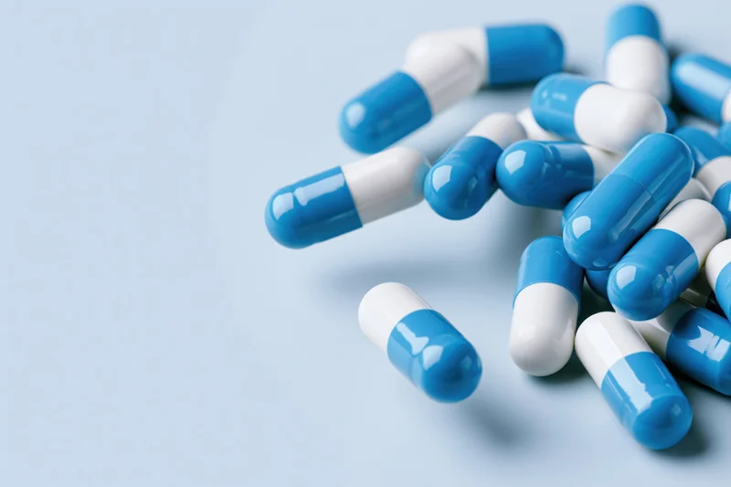 Blue and white pharmaceutical capsules scattered on a light blue surface