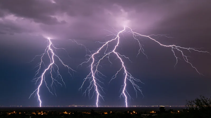 Multiple lightning bolts striking across a dark sky above a city at night