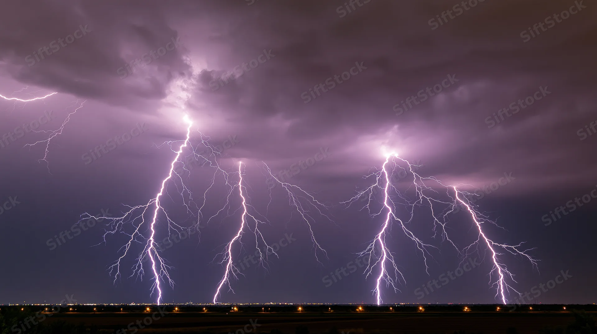 Multiple lightning bolts striking simultaneously across a wide night sky above a distant cityscape