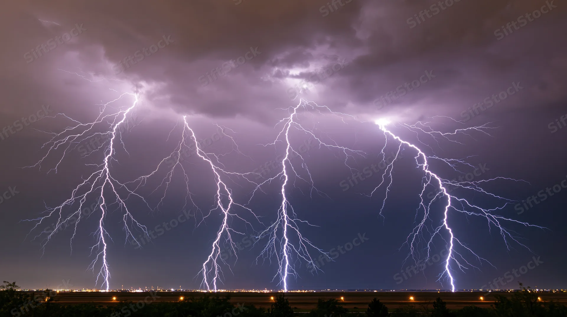 Multiple lightning bolts striking across a dark sky above a cityscape at night