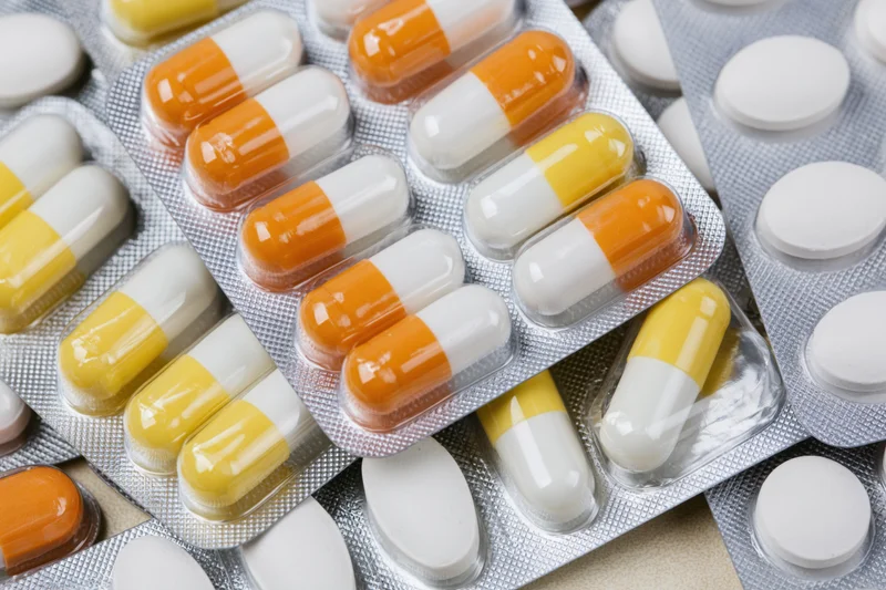 Multiple pharmaceutical blister packs filled with orange-white and yellow-white capsules arranged in overlapping layers