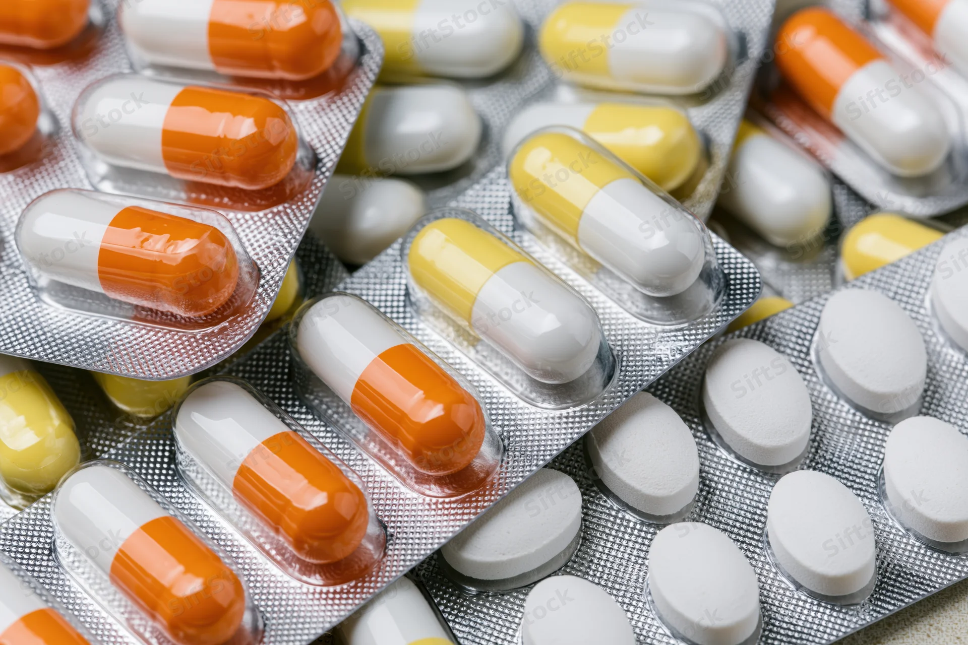 Multiple pharmaceutical blister packs filled with orange-white and yellow-white capsules and white tablets, close-up view