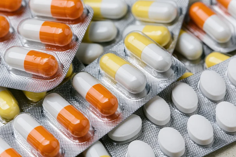 Multiple pharmaceutical blister packs filled with orange-white and yellow-white capsules and white tablets, close-up view