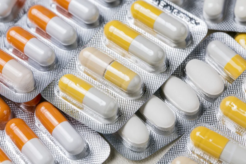 Multiple pharmaceutical blister packs filled with orange-white and yellow-white capsules arranged in overlapping layers