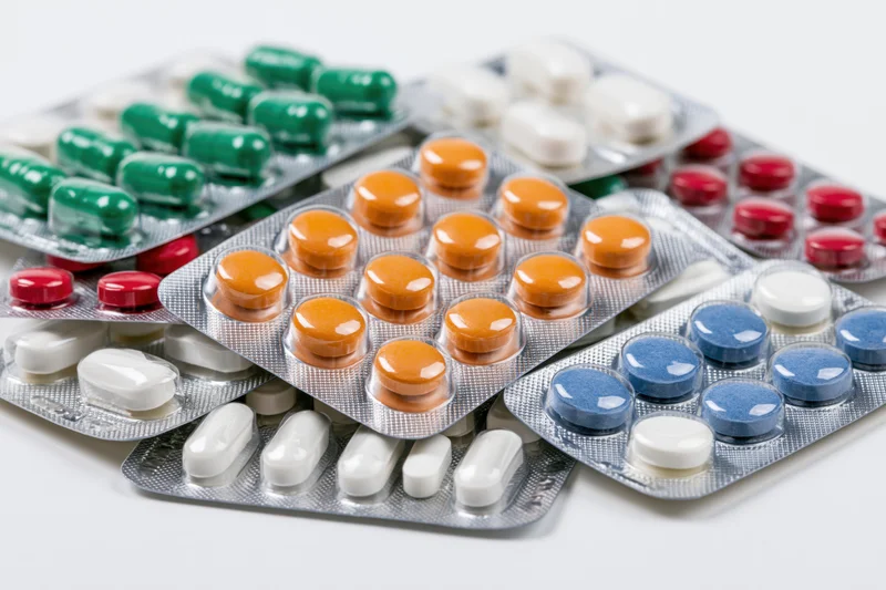 Multiple pharmaceutical blister packs scattered on a white surface containing colorful pills and capsules