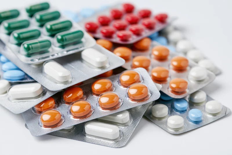 Multiple pharmaceutical blister packs scattered on a white surface containing colorful pills and capsules