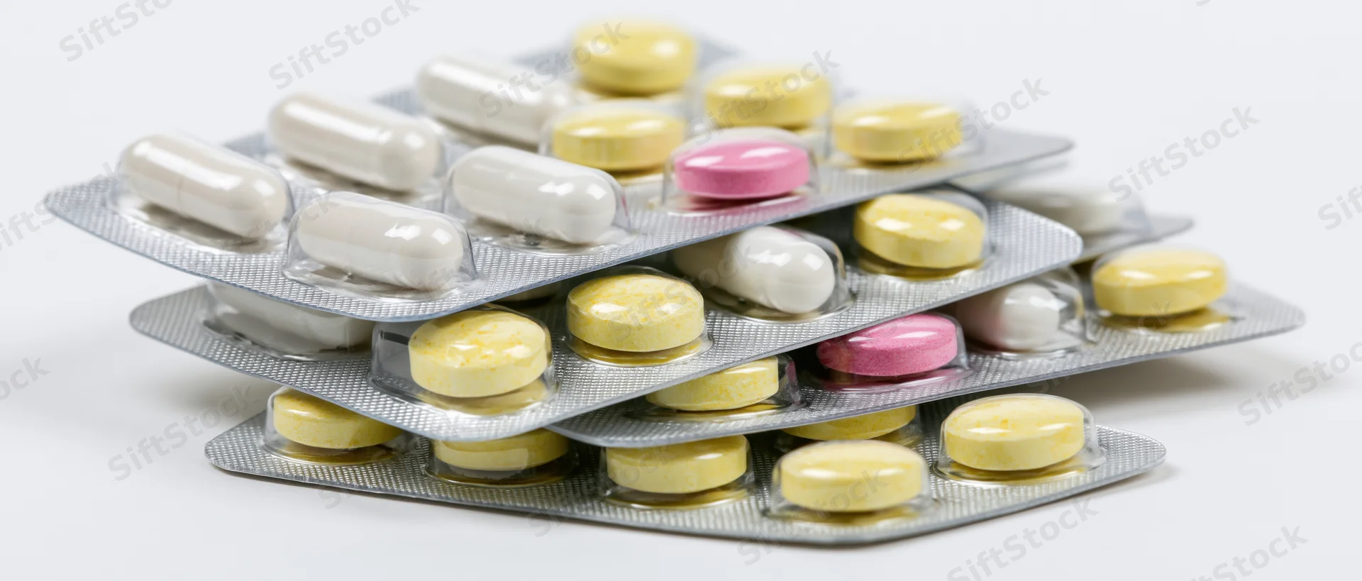 Stacked pharmaceutical blister packs with tablets and capsules on white background