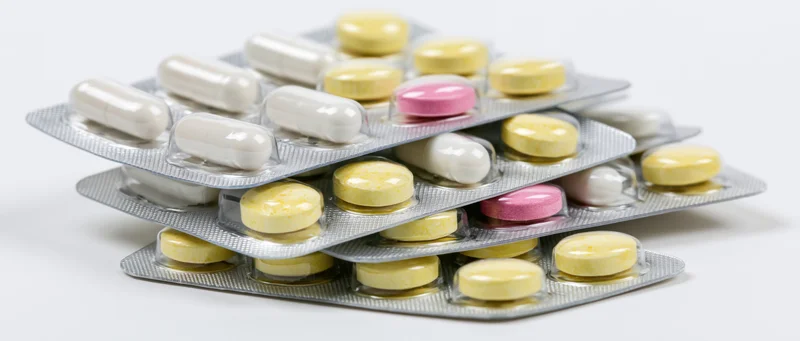 Stacked pharmaceutical blister packs with tablets and capsules on white background