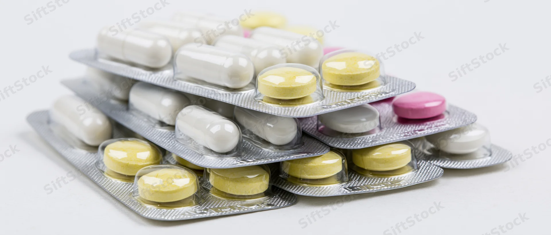 Stacked pharmaceutical blister packs with white capsules and yellow tablets on white background