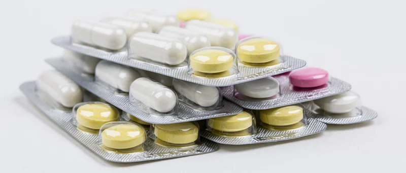 Stacked pharmaceutical blister packs with white capsules and yellow tablets on white background