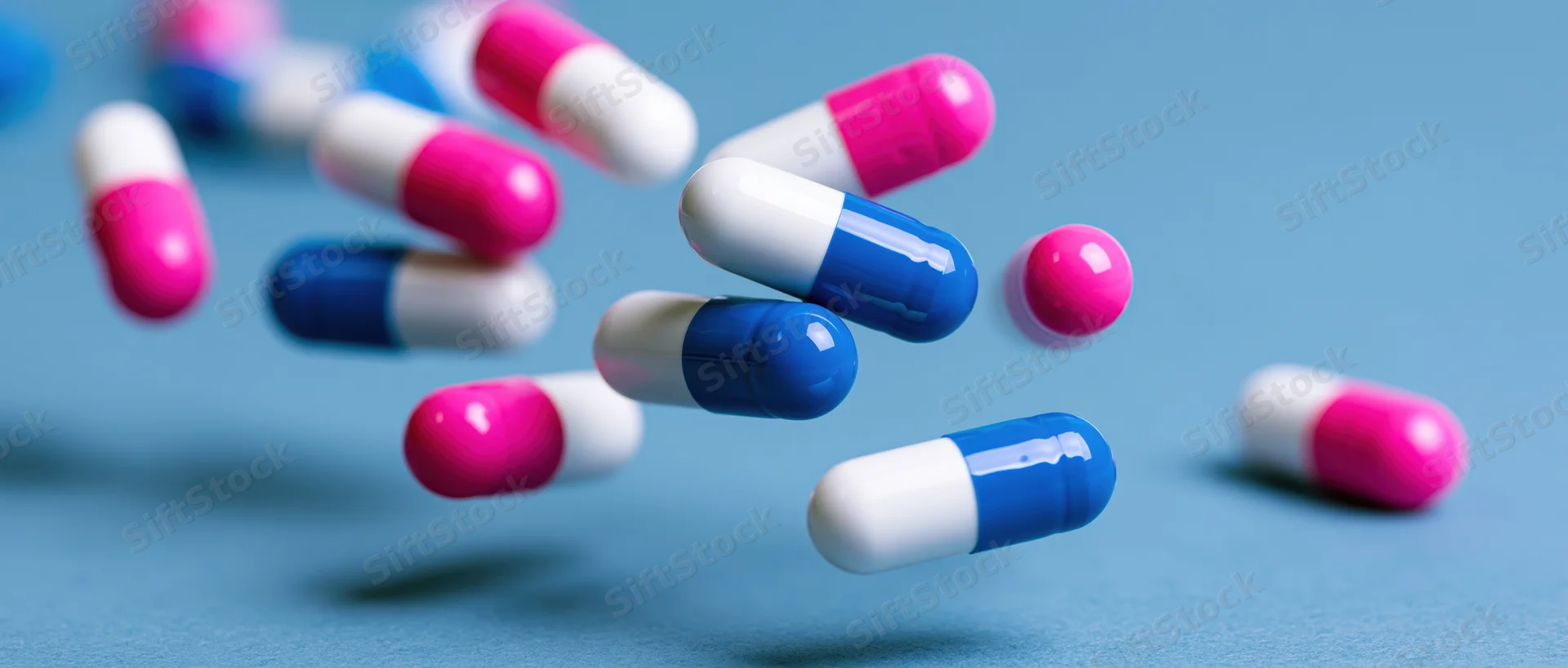 Pharmaceutical capsules in mid-air against a blue background