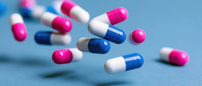 Pharmaceutical capsules in mid-air against a blue background