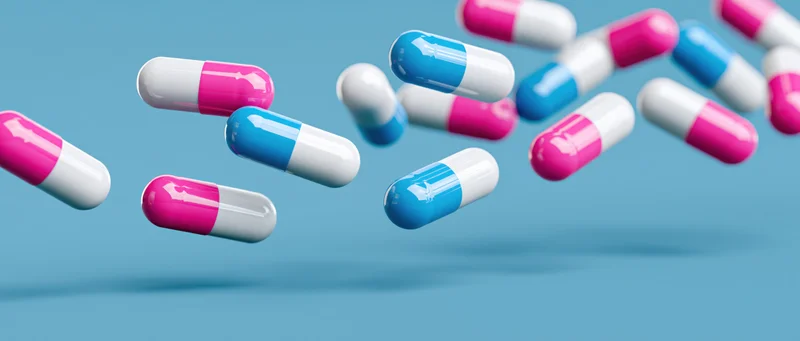 Floating pharmaceutical capsules in pink and blue against a light blue background