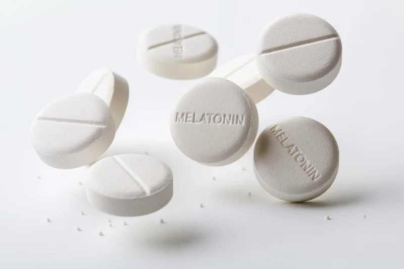 White melatonin supplement tablets scattered mid-air on a plain white surface
