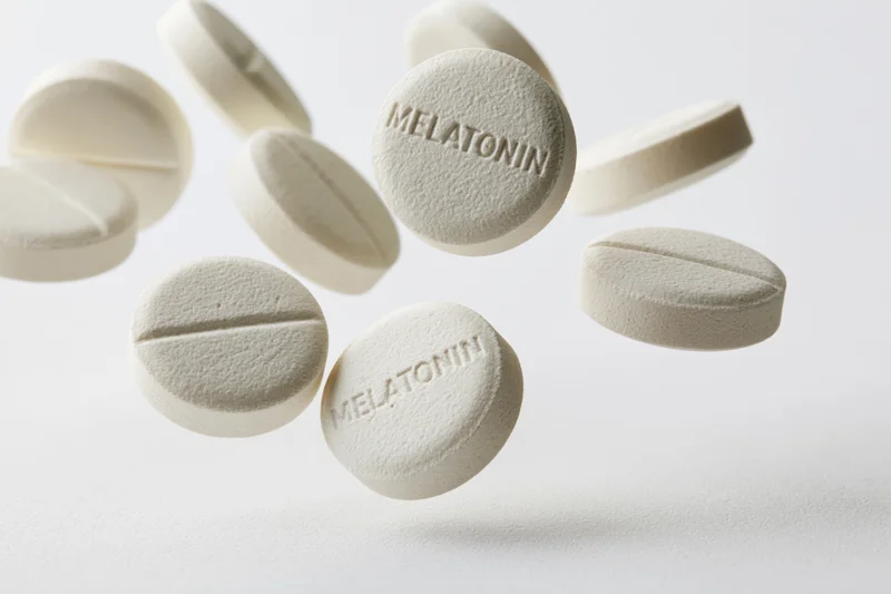 White melatonin supplement tablets floating midair against a plain white background