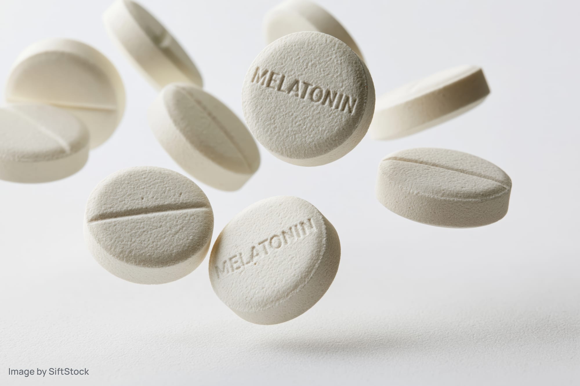 White melatonin supplement tablets floating midair against a plain white background