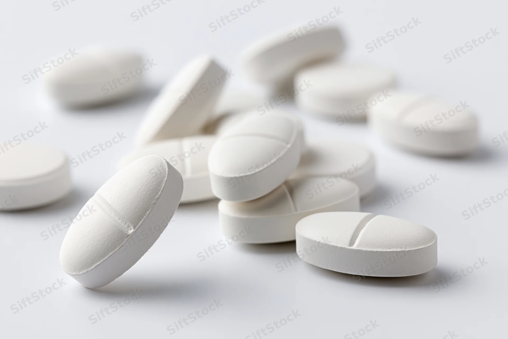 White oval and round pharmaceutical tablets scattered on a plain white surface