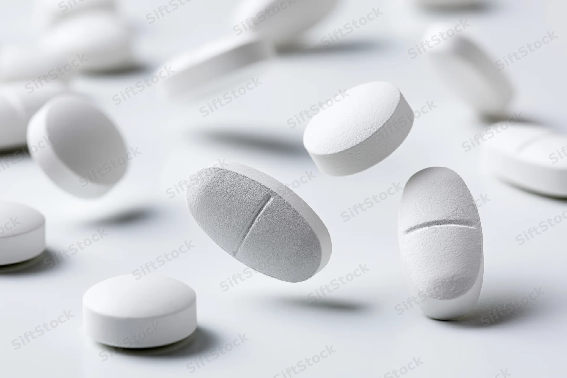White oval and round pharmaceutical tablets scattered on a plain surface