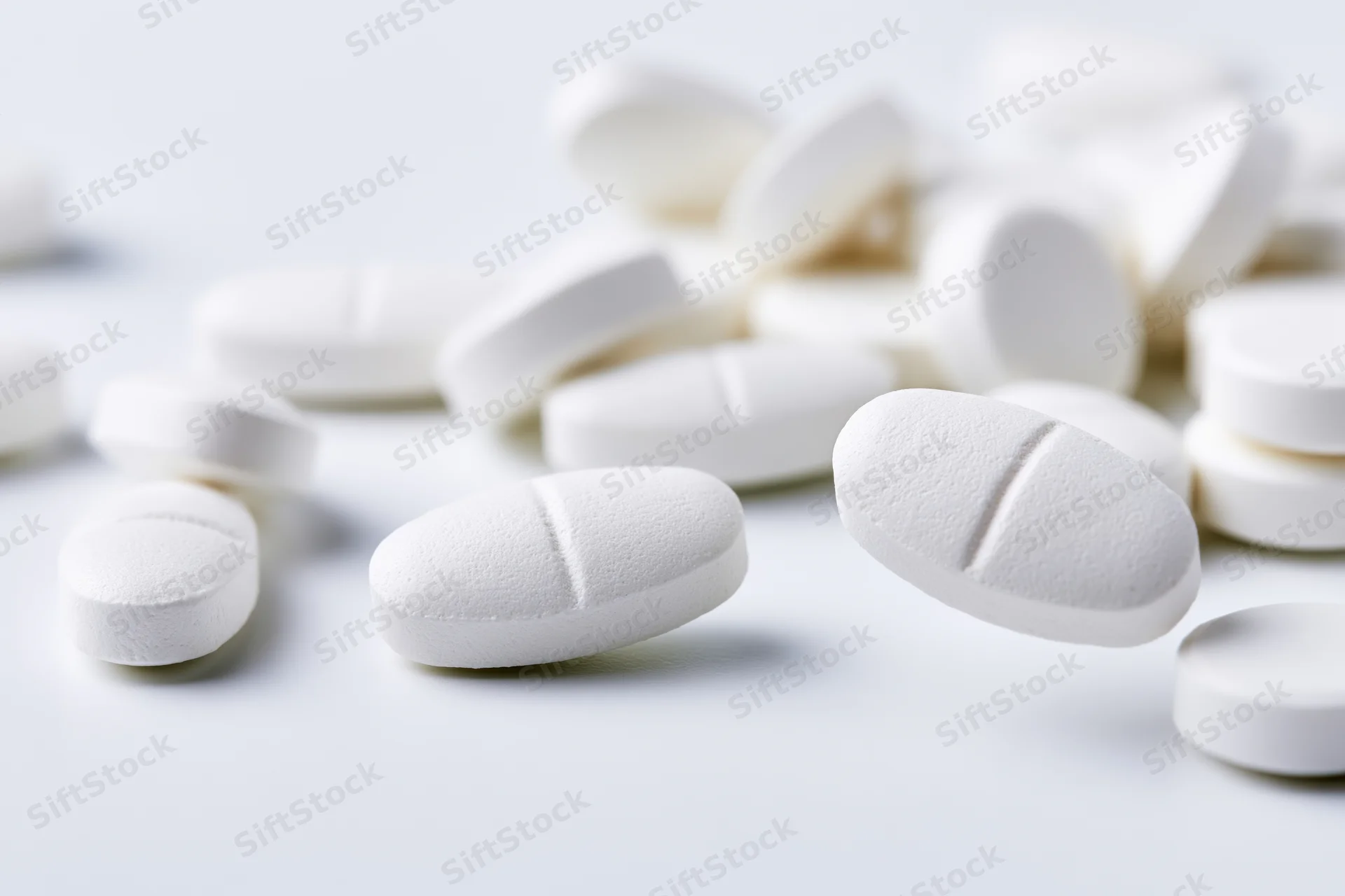 White oval and round pharmaceutical tablets scattered on a plain surface
