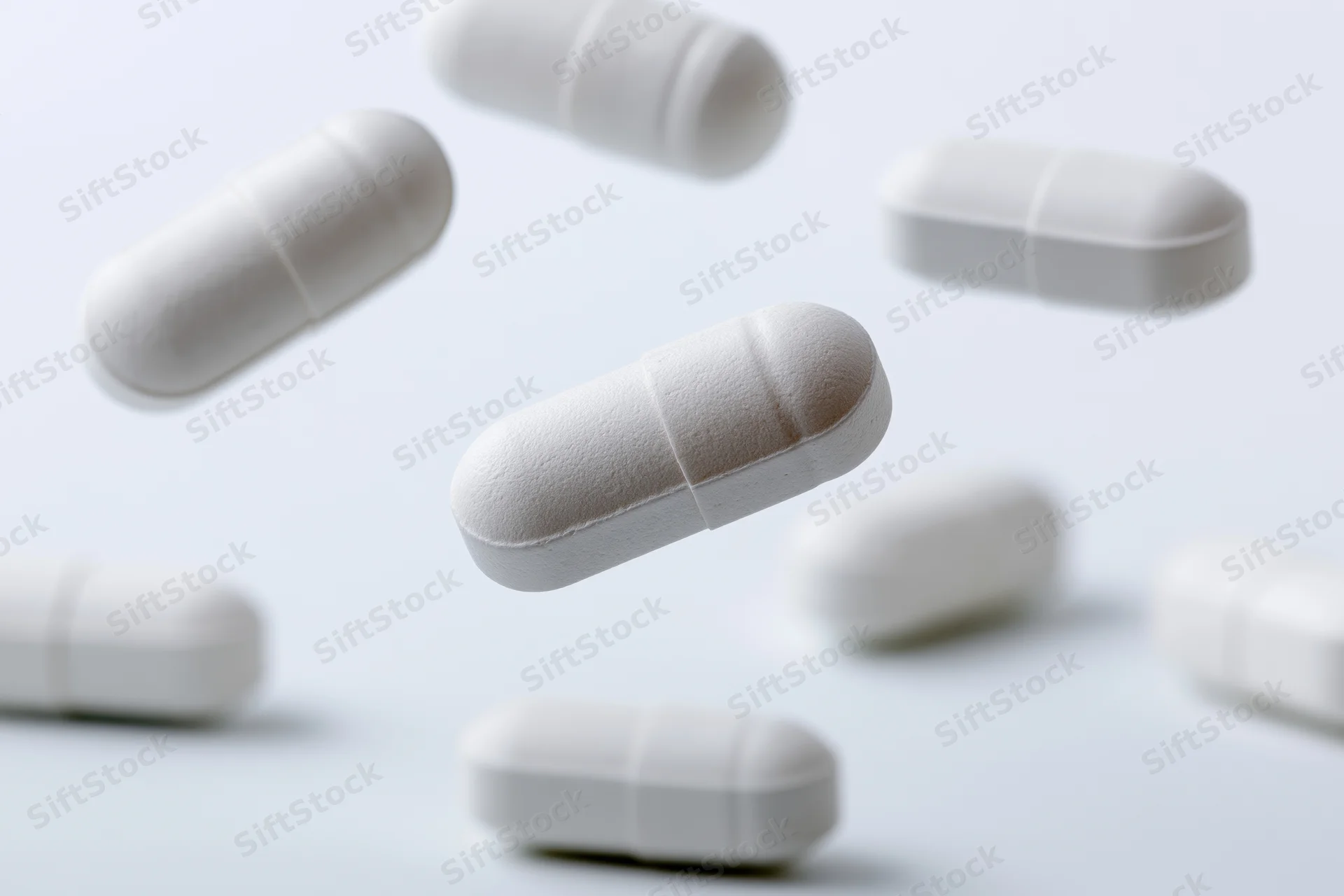 White oval medication capsules floating and scattered against a plain white background