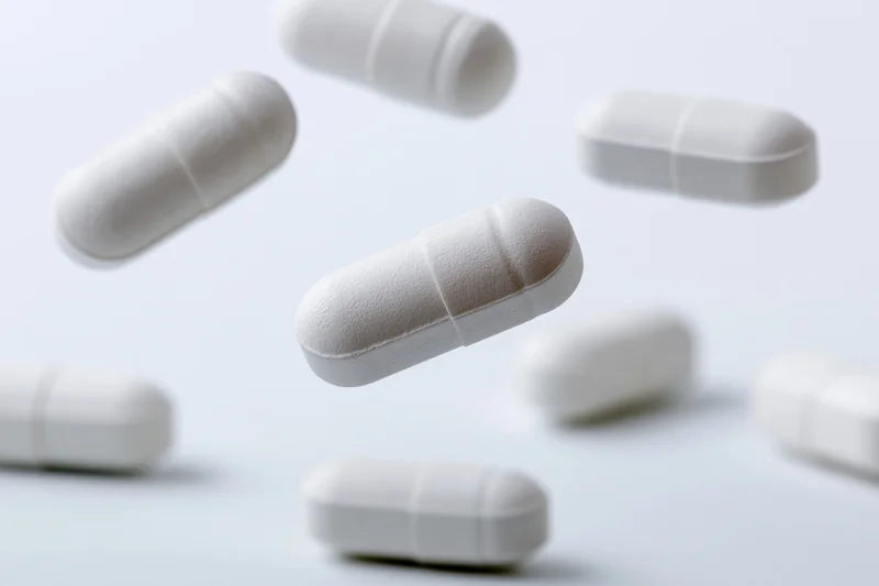 White oval medication capsules floating and scattered against a plain white background