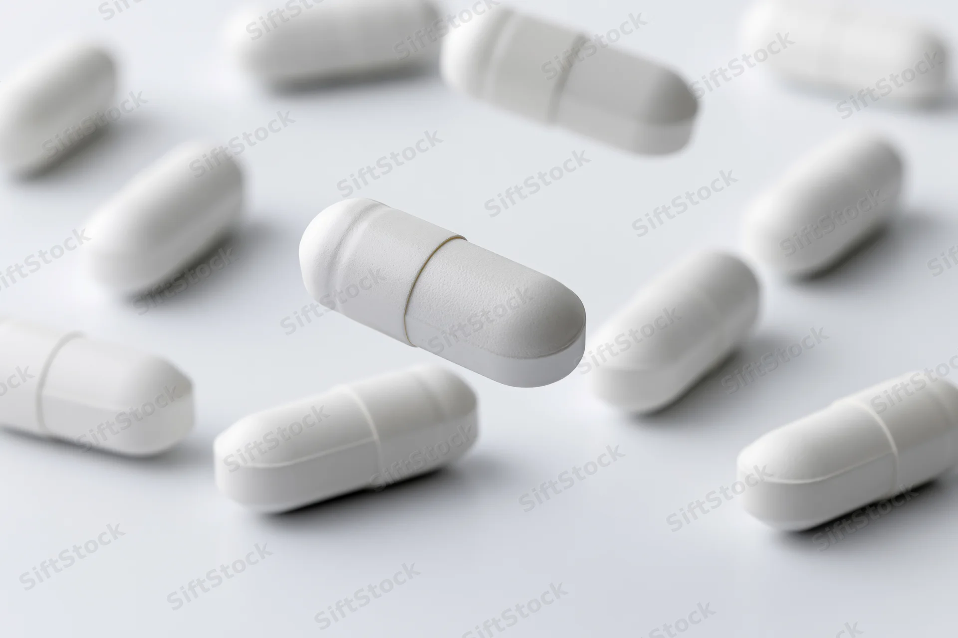 White medication capsules scattered and floating on a plain white surface