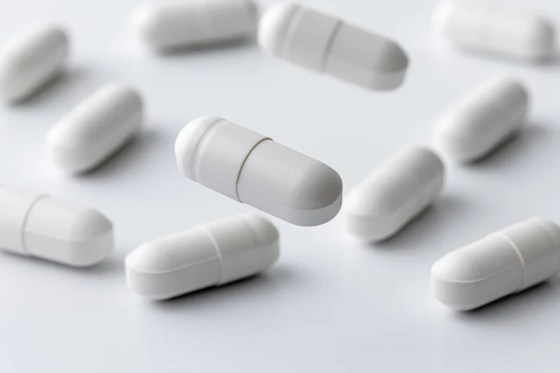 White medication capsules scattered and floating on a plain white surface