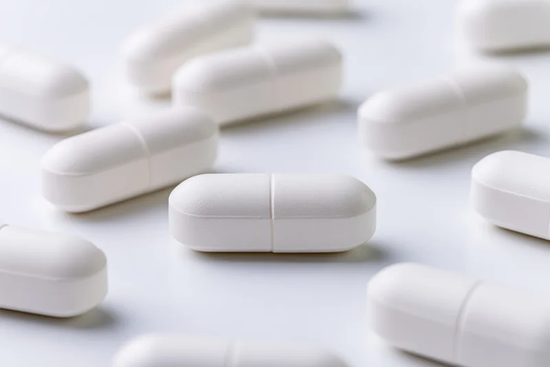 White oval medication capsules scattered on a plain white surface