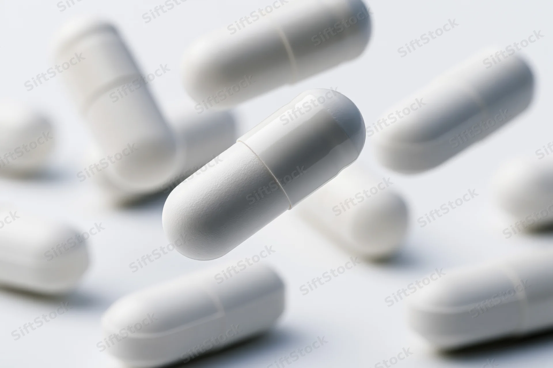 White medication capsules floating and scattered on a plain surface