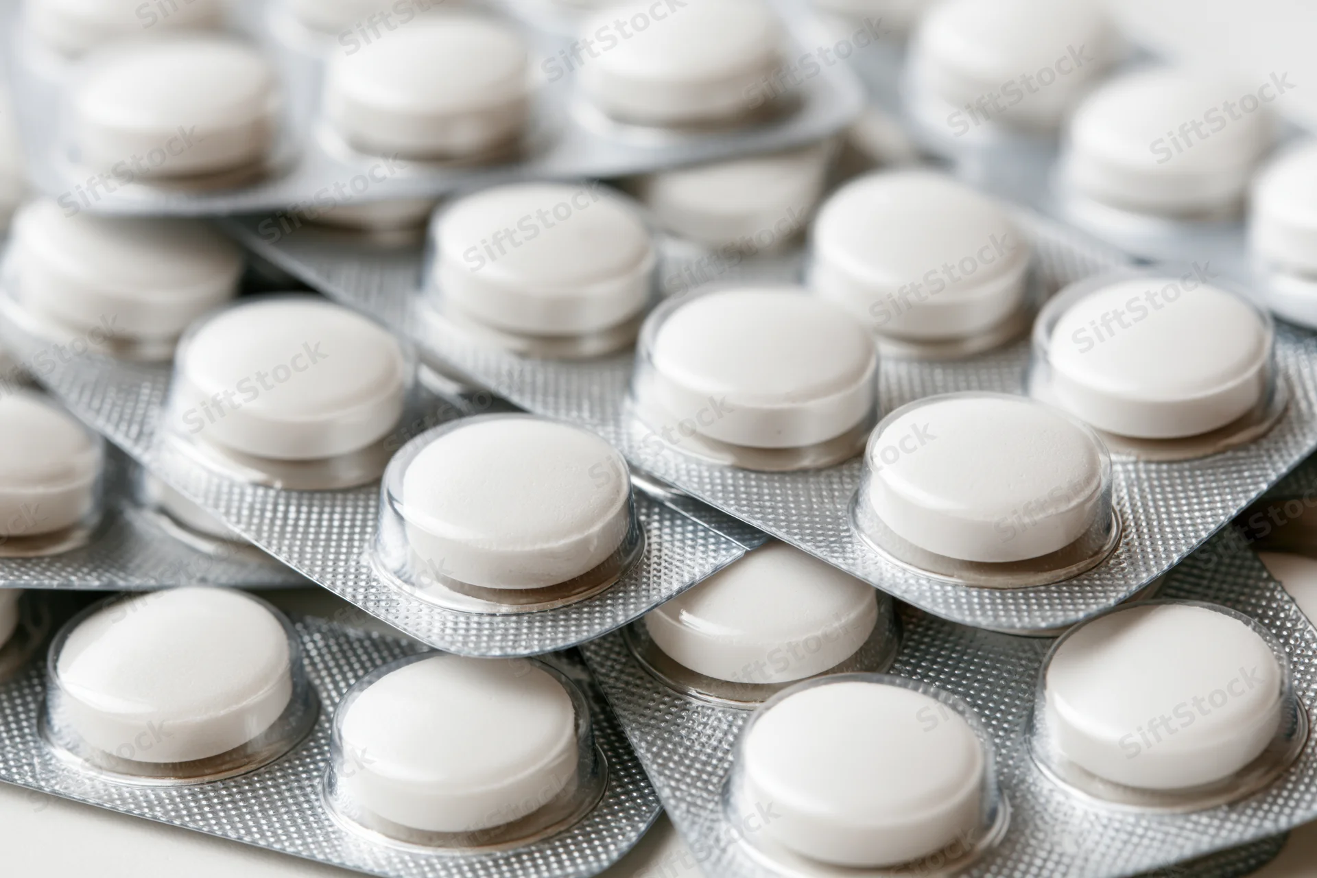 White round pills in blister packs stacked and layered on a light surface