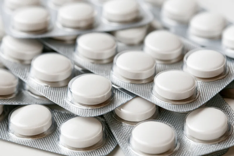 White round pills in blister packs stacked and layered on a light surface