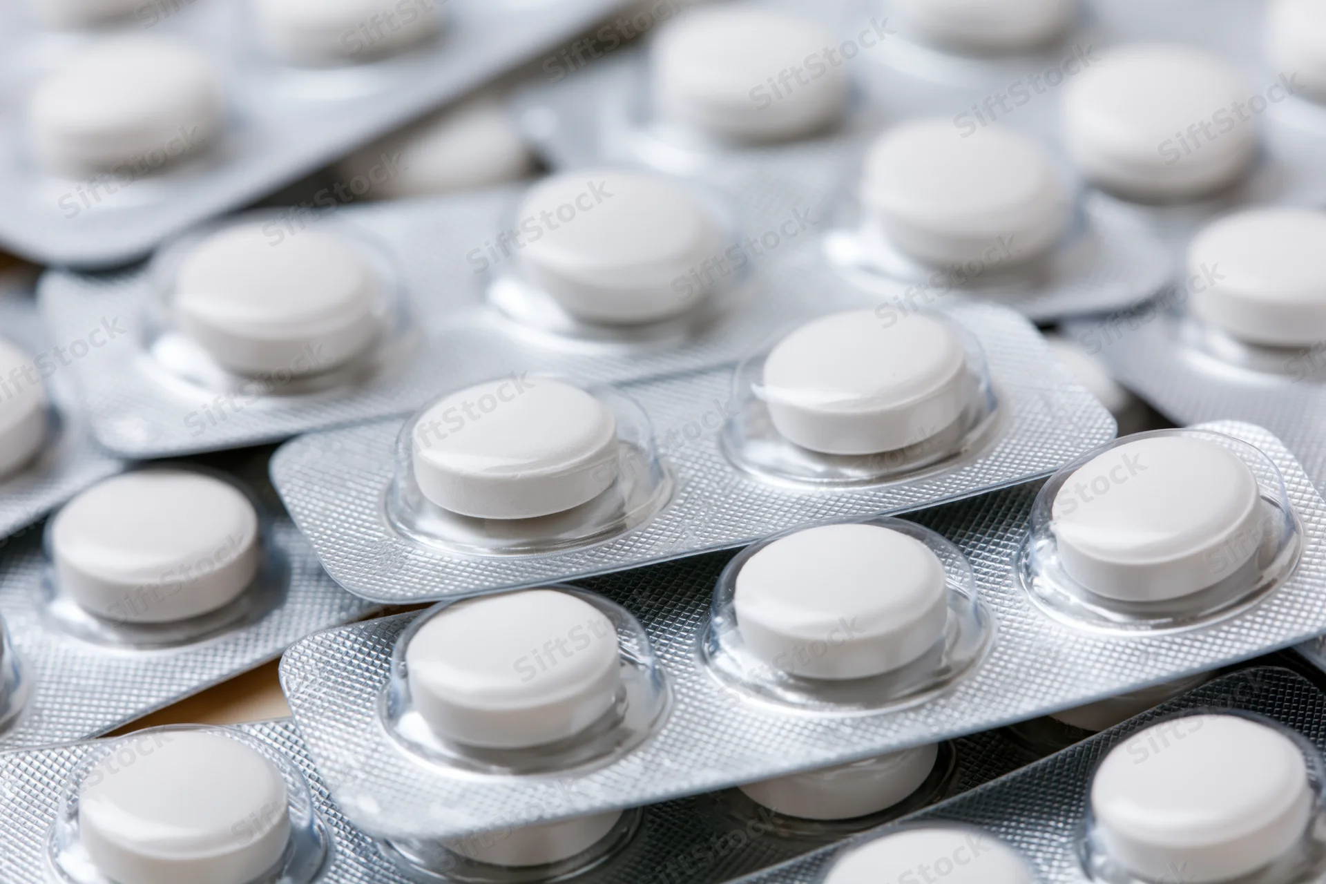 Multiple white round pills in blister packs stacked and layered on a reflective surface